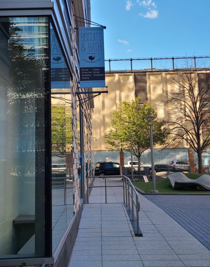 external of a battery park dog daycare storefront with a ramp, a blue banner